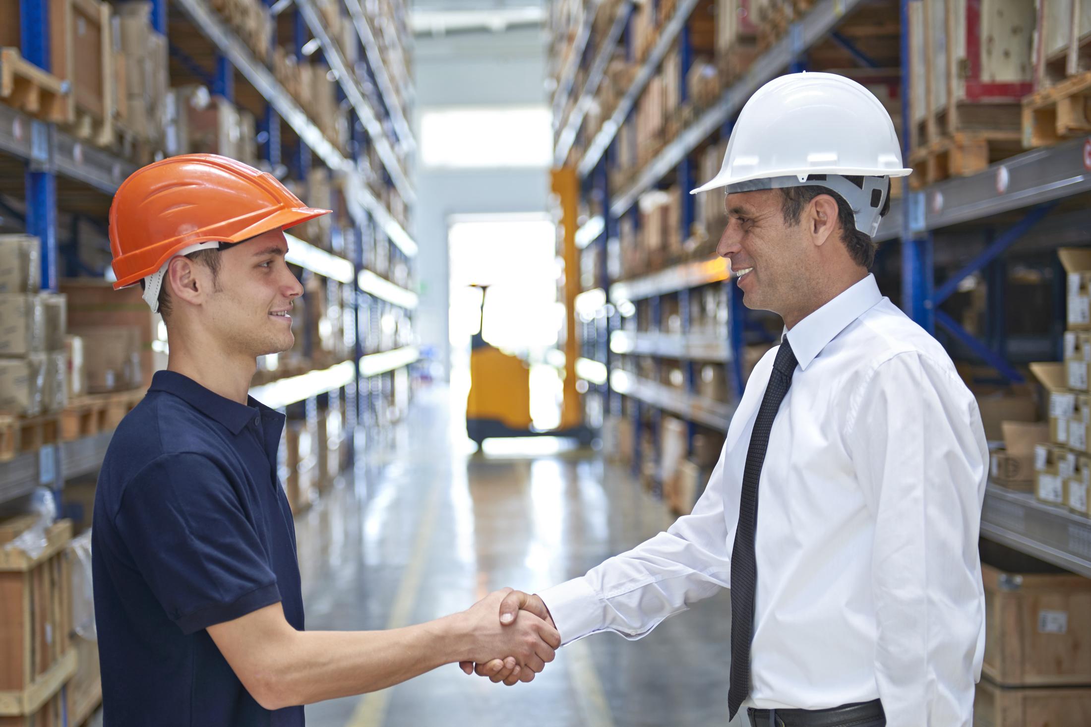 Two men shaking hands in a warehouse wearing hard hats