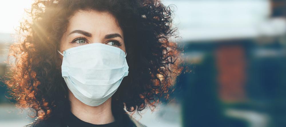 Lovely curly haired lady protecting herself from viruses while wearing special mask