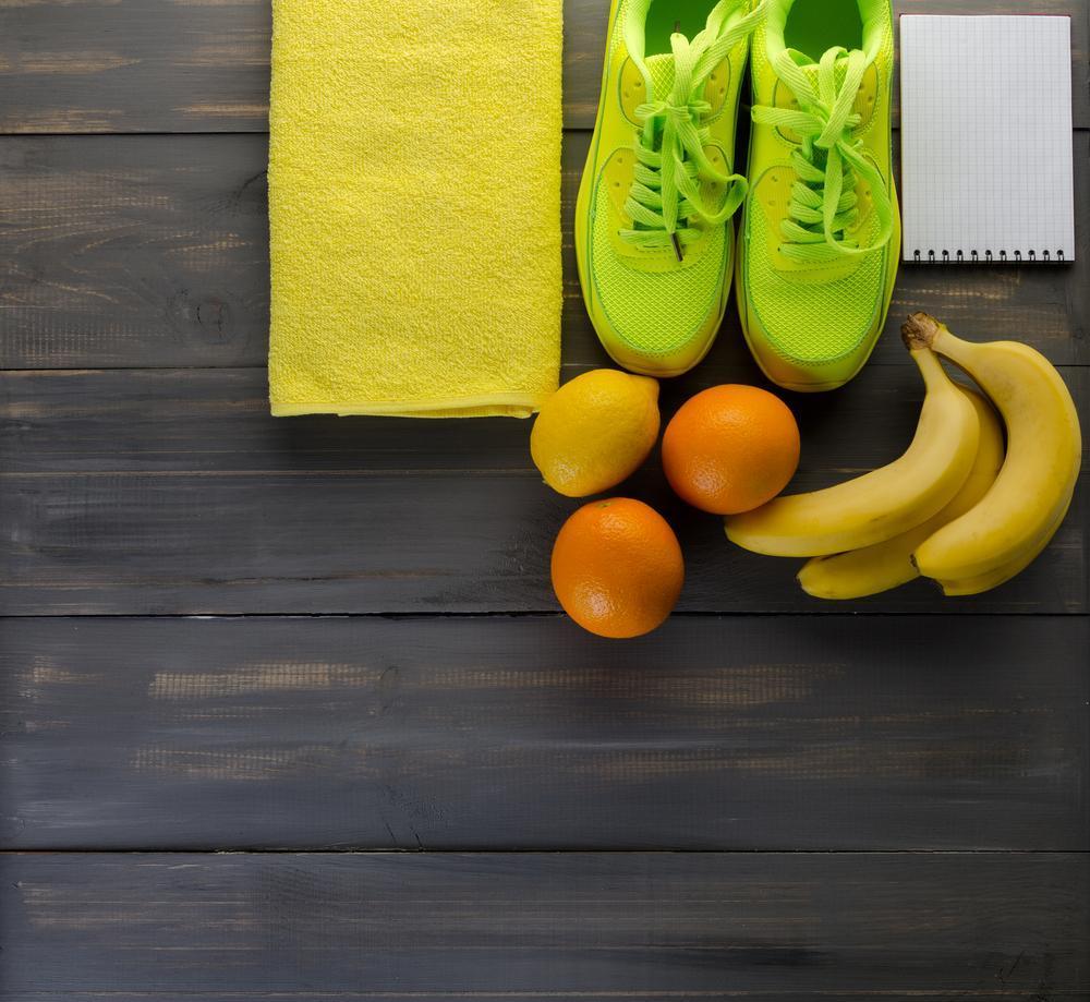 Fitness concept with sneakers towel bananas oranges and lemons on black wooden background