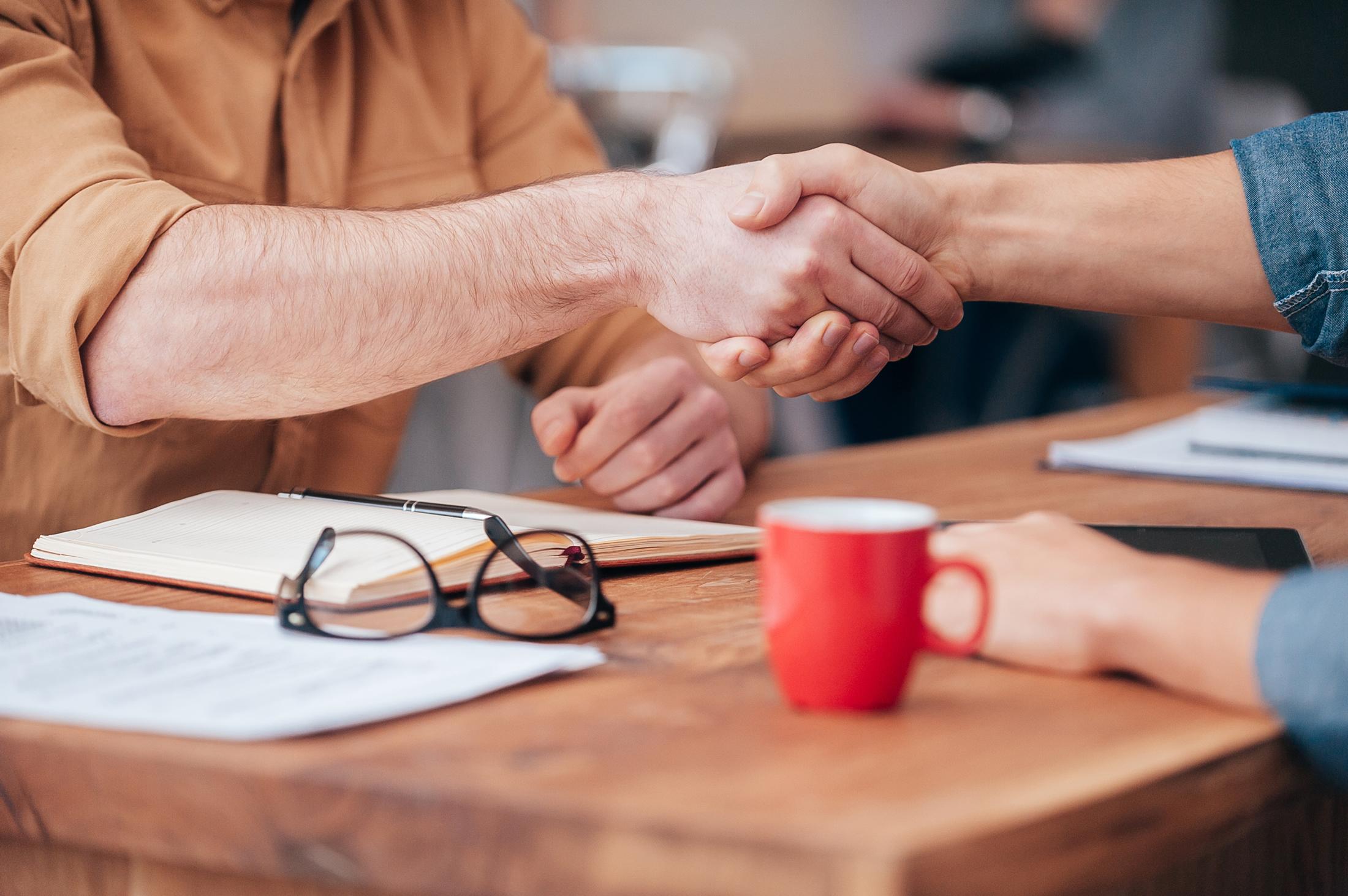 Two colleagues shaking hands over coffee at a wooden table