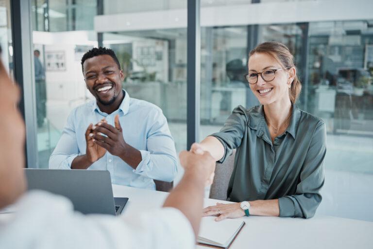 A man is mid-applause while a woman reaches out to shake a 3rd person's hand, resembling an onboarding process